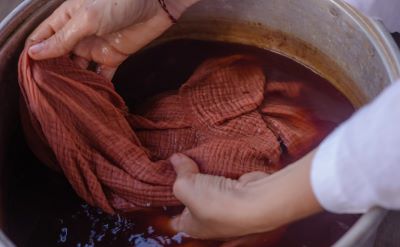 Mani che tingono un tessuto di colore rosso all'interno di un contenitore pieno di colorante liquido